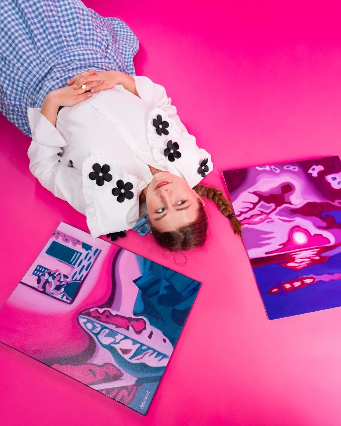 Salomé Quetier ou Slalomart pose allongée avec ses peintures à l'huile originales "La vie en rose" et "Intérieur rose" dans sa bichromie signature